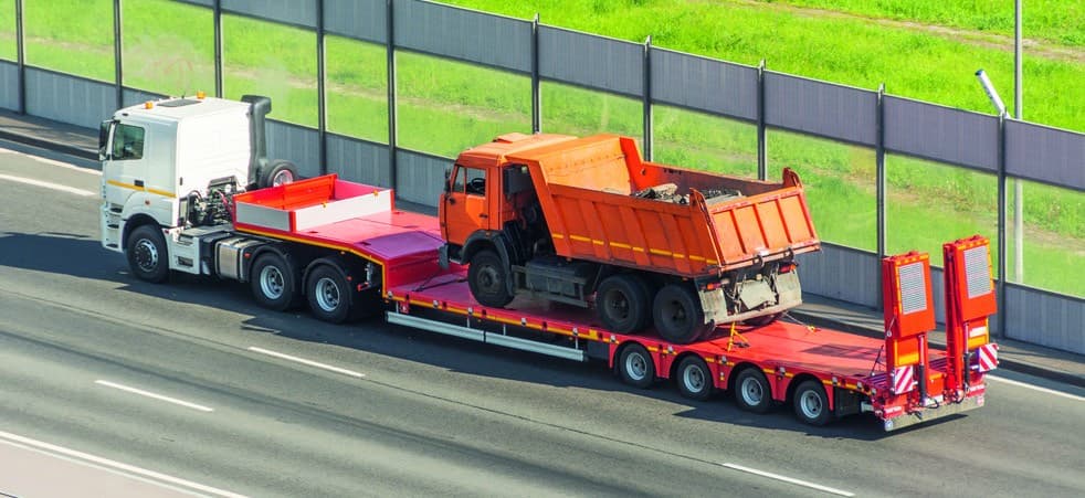 Heavy equipment being transported on a lowbed trailer for a contractor works project.